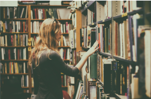 Mulher escolhendo um livro na prateleira de uma biblioteca
